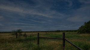 Rural landscape with a wooden fence and open field under a blue sky.